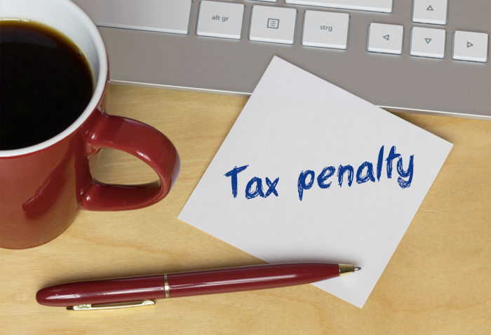 Tax Penalty Desk with a cup of coffee, a red pen, the bottom of a keyboard, and a Post-It note that says 'tax penalty'